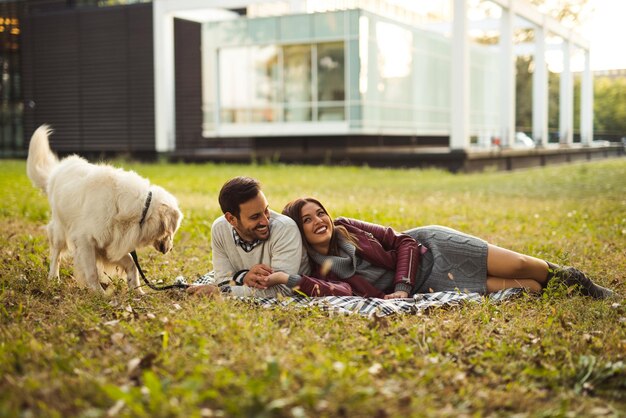 Glückliches Paar, das mit seinem Hund auf dem Gras im Park liegt