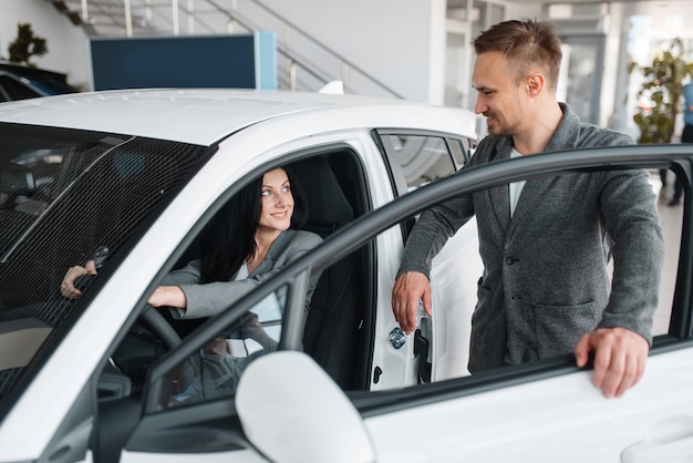 Glückliches Paar, das neues Auto im Ausstellungsraum kauft, Frau hinter dem Lenkrad.