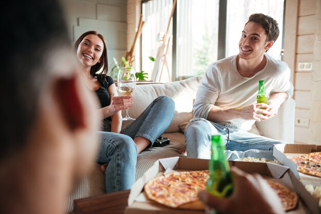 Glückliches Paar, das Pizza isst, Bier und Wein mit Freunden trinkt