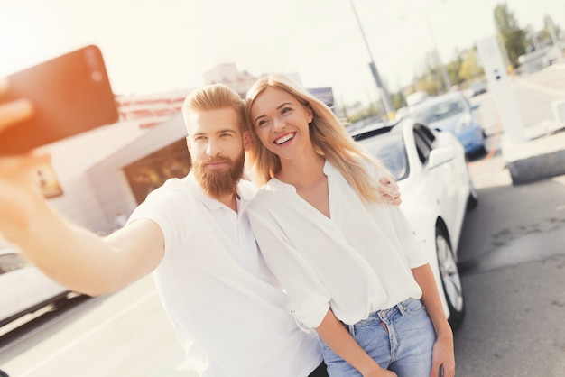 Glückliches Paar, das Selfie vor Auto tut