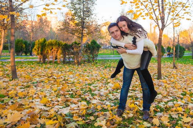 Glückliches Paar, das Spaß im Herbstpark an einem sonnigen Falltag hat