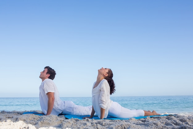 Glückliches Paar, das Yoga neben dem Wasser tut