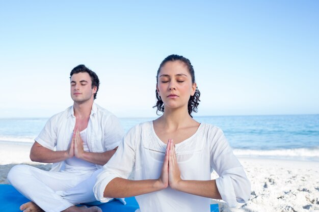 Glückliches Paar, das Yoga neben dem Wasser tut