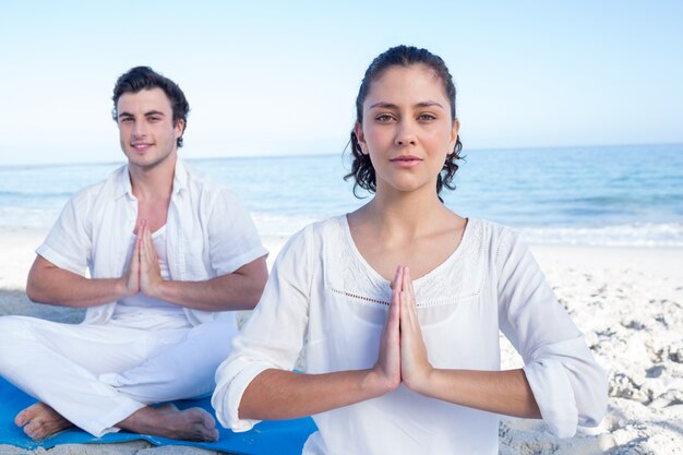 Glückliches Paar, das Yoga neben dem Wasser tut