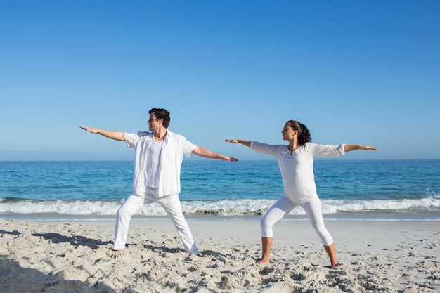 Glückliches Paar, das Yoga neben dem Wasser tut