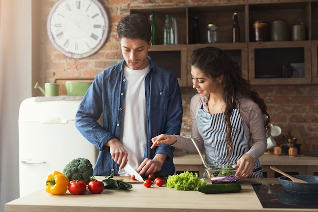 Glückliches Paar, das zu Hause gesundes Abendessen in ihrer Dachbodenküche kocht. Gemüsesalat zubereiten.