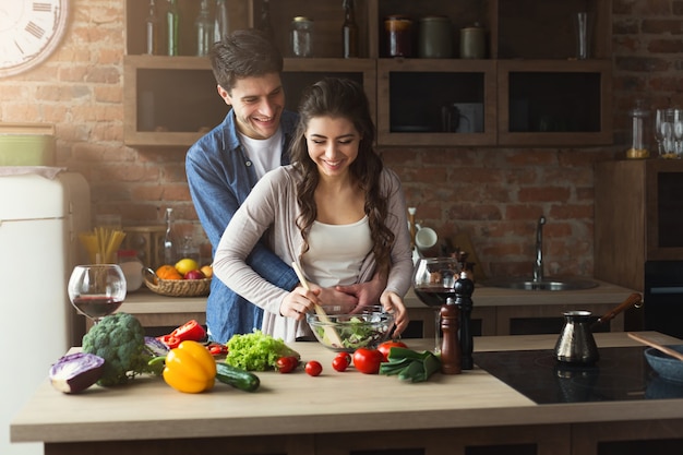 Glückliches Paar, das zu Hause in ihrer Loft-Küche zusammen Abendessen kocht. Gemüsesalat zubereiten.