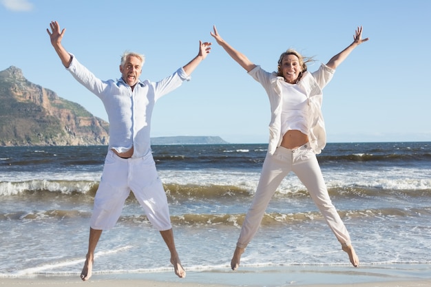 Glückliches Paar, das zusammen auf den Strand springt