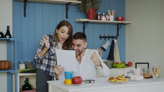 glückliches paar erhält gute nachrichten, die sich in der küche entfalten, während sie zu hause frühstücken