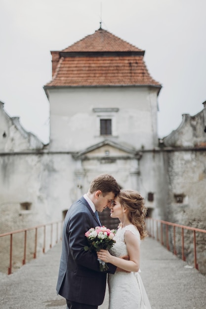 Glückliches Paar frisch verheirateter Paare, die in der Nähe des märchenhaften Hochzeitsmoments des Schlosses posieren. Schöne Braut und Bräutigam umarmen sich in der Nähe des alten Schlosseingangs in Europa