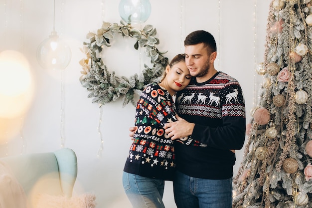 Glückliches Paar im traditionellen Pullover, das den Weihnachtsbaum zusammen zu Hause schmückt