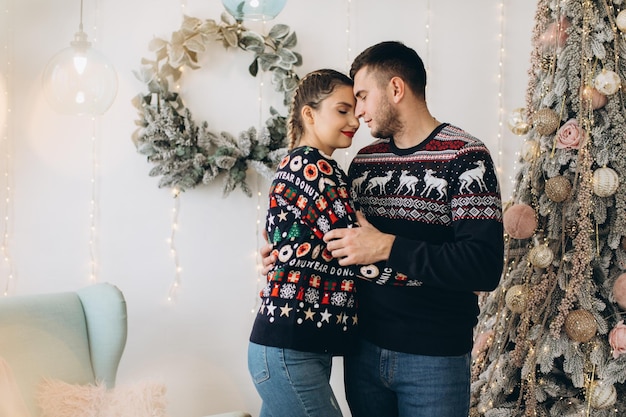 Glückliches Paar im traditionellen Pullover, das den Weihnachtsbaum zusammen zu Hause schmückt