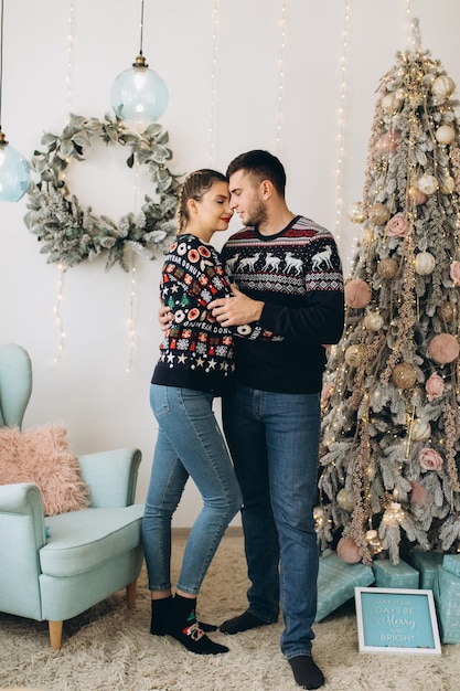 Glückliches Paar im traditionellen Pullover, das den Weihnachtsbaum zusammen zu Hause schmückt