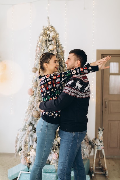 Glückliches Paar im traditionellen Pullover, das den Weihnachtsbaum zusammen zu Hause schmückt