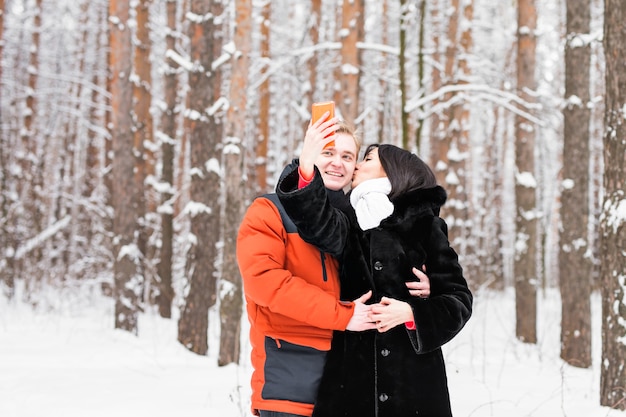 Glückliches Paar im Winter, das Fotos von sich selbst mit Smartphone macht.