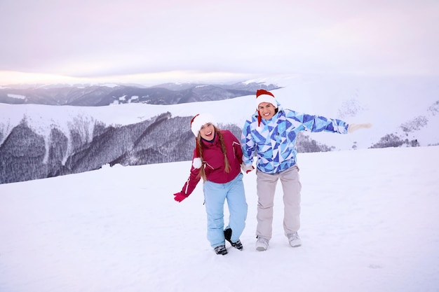 Glückliches Paar in Weihnachtsmützen, das Spaß im verschneiten Resort hat. Winterurlaub