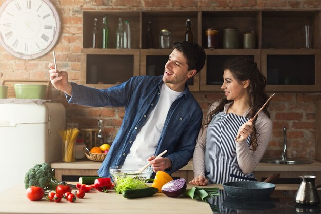 Glückliches Paar kocht Abendessen und macht Selfie in ihrer Loft-Küche zu Hause. Gemüsesalat zubereiten.