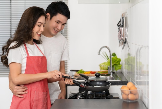 Glückliches Paar kocht und bereitet Essen in der Küche zu Hause zu Mann umarmt Frau