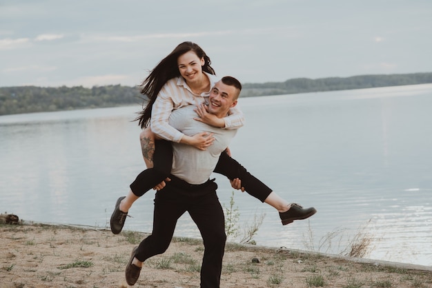 Glückliches Paar Mädchen und Kerl, die Spaß am Strand am Fluss im Sommer haben. Das Foto ist aufgrund von Bewegung und kurzer Verschlusszeit verschwommen