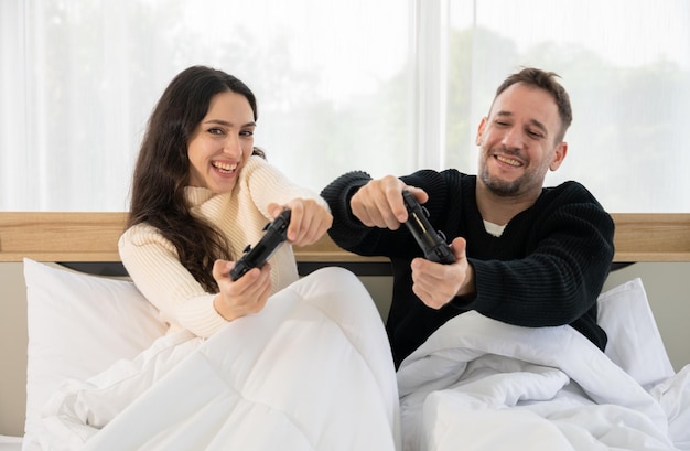 Glückliches Paar, Mann und Frau, die Spaß haben, während sie gemeinsam im Bett Videospiele spielen