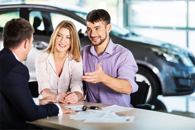 Glückliches Paar mit Autohändler in der Autoshow oder im Salon