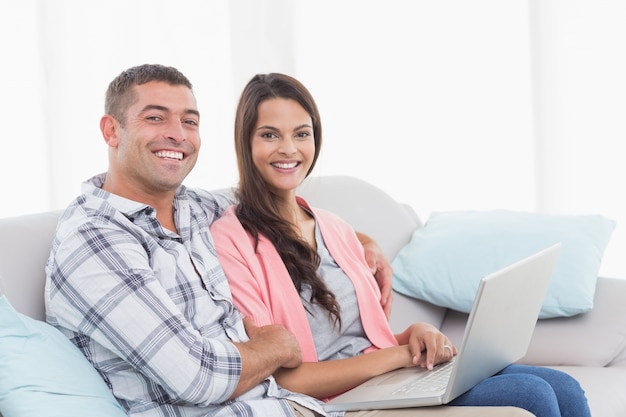 Glückliches Paar mit dem Laptop, der auf Sofa sitzt