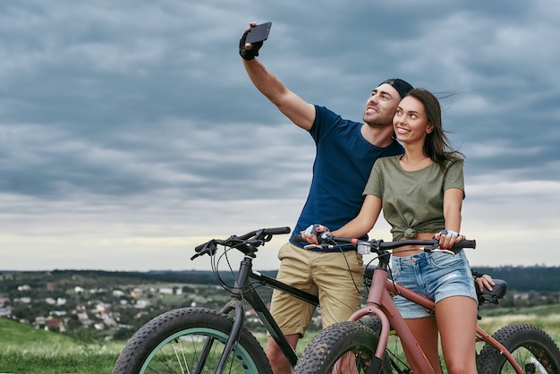 Glückliches Paar mit Fatbikes, die im Freien ein Selfie mit dem Smartphone machen