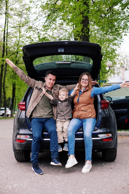 Glückliches Paar mit ihrem kleinen Sohn im offenen Kofferraum des Geländewagens auf dem Parkplatz