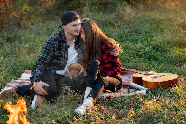 Glückliches Paar mit ihrem lustigen Hund, der auf dem Rasen im Frühlingspark sitzt.