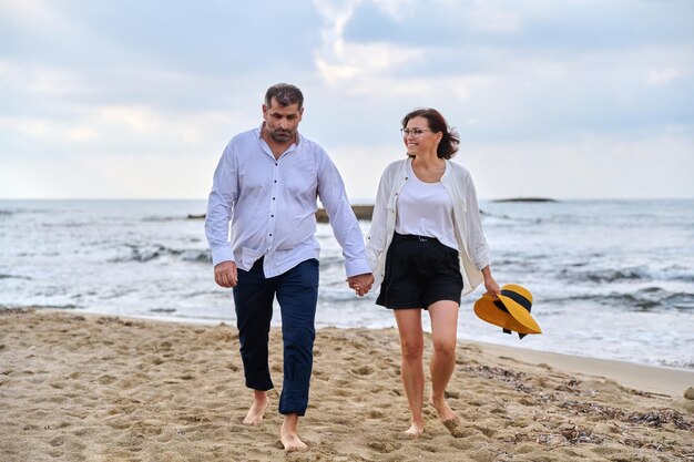 Glückliches Paar mittleren Alters, das zusammen am Strand spazieren geht