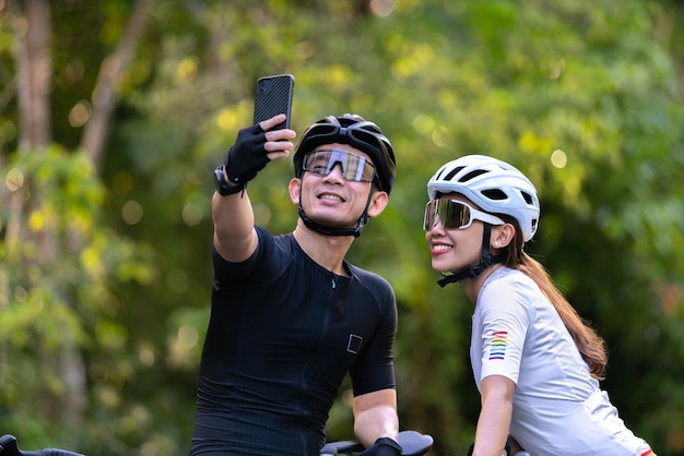 Glückliches Paar radelt Selfie mit Smartphone während der Fahrt auf dem Land für einen gesunden Lebensstil