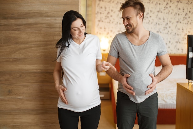 Glückliches Paar, schwangere Frau mit Bauch zu Hause. Schwangerschaft, pränatale Periode. Werdende Mama und Papa ruhen sich auf dem Sofa aus, Gesundheitsvorsorge