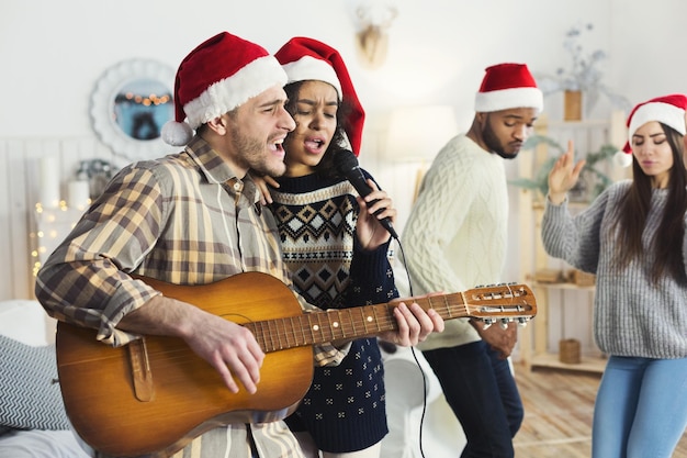 Glückliches Paar singt Duett auf der Weihnachtsfeier, hat Spaß mit Freunden, kopiert Raum