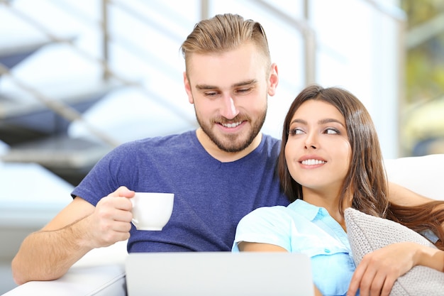 Glückliches Paar sitzt auf dem Sofa mit Kaffee und arbeitet an einem Laptop