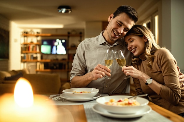 Glückliches Paar umarmt und stößt mit Champagner an, während es am Esstisch zu Abend isst