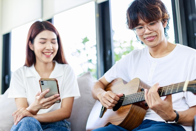 Glückliches Paar zu Hause Ein junger Mann, der Freundin im Wohnzimmer Gitarre spielt Freizeitaktivitäten