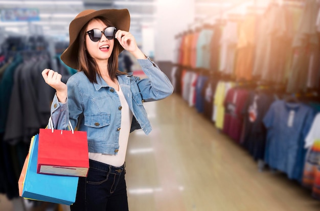 Glückliches Porträt, schöne junge Frau, lächelnd, stehend mit Sonnenbrille und Hut, sie erregte das Halten von Einkaufstaschen in mehreren Farben auf dem Einkaufszentrum mit Kopierraum, Black Friday-Verkaufskonzept