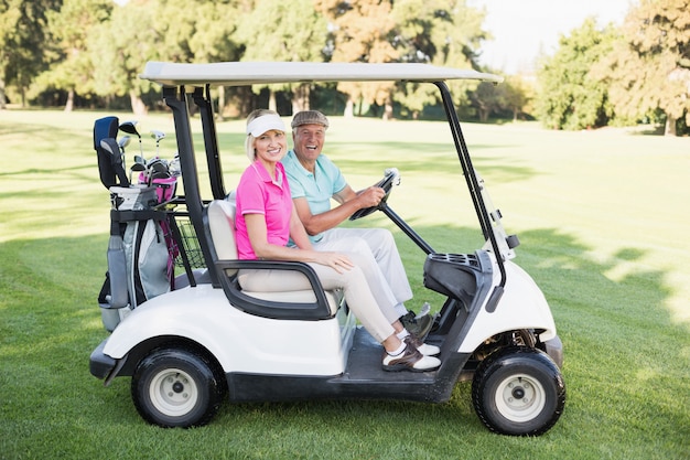 Foto glückliches reifes paar, das im golfbuggy sitzt