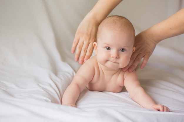 Glückliches Säuglingsmädchen, das zu Hause Babymassage von seiner Mutter tut. Neugeborenes Kind ca. 5 Monate alt