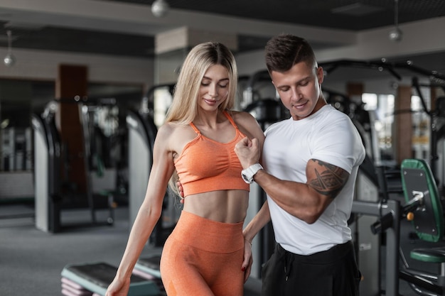 Glückliches schönes Fitness-Paar mit einem schlanken muskulösen Körper, das in der Turnhalle posiert Schöne sexy Frau mit einem Fitness-Trainer