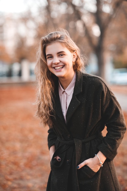 Glückliches schönes jugendlich Mädchen, das Herbstjacke trägt, die über gefallenes Laub lacht