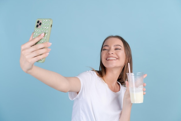 Glückliches schönes Mädchen fotografiert sich mit frischem Milchshake auf dem Handy