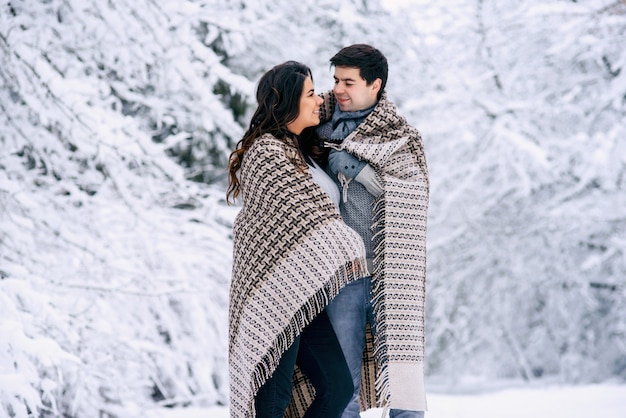 Glückliches schönes Paar bedeckt mit einer warmen Decke und geht in einem verschneiten Park