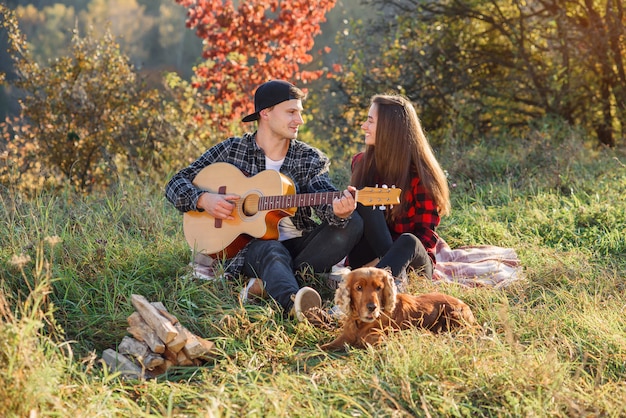 Glückliches schönes Paar mit Gitarre und ihrem Hund, die sich auf einem Picknick ausruhen