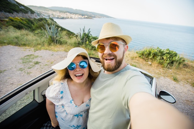 Glückliches schönes verliebtes Paar, das ein Selfie-Porträt macht, das im Urlaub ein Cabrio-Auto auf der Straße fährt Mietwagen und Urlaub