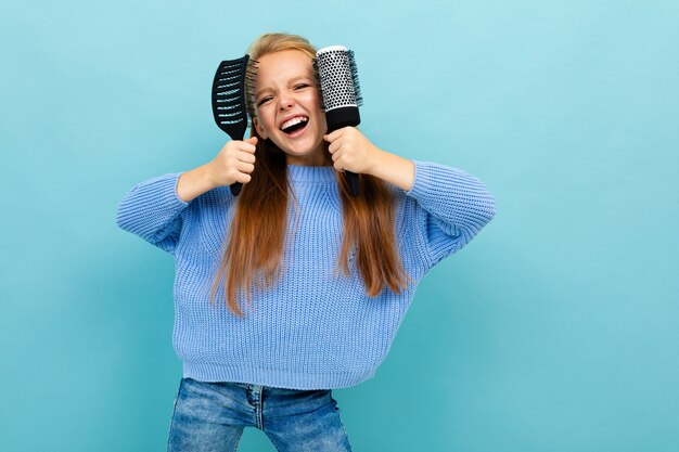 Glückliches Schulmädchen, das herum mit Kämmen in ihren Händen gegen eine blaue Wand täuscht