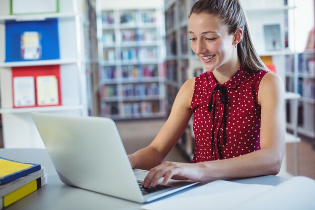 Glückliches Schulmädchen, das Laptop in Bibliothek verwendet