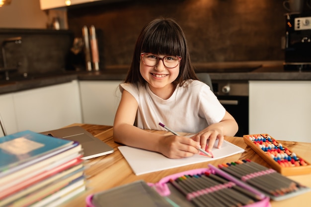 Glückliches Schulmädchen macht Hausaufgaben zu Hause. Online-Lernen ohne digitale Geräte. Fernunterricht, Homeschooling