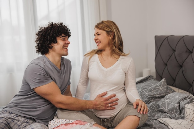 Glückliches schwangeres Paar, das im Schlafzimmer spricht und sich entspannt.