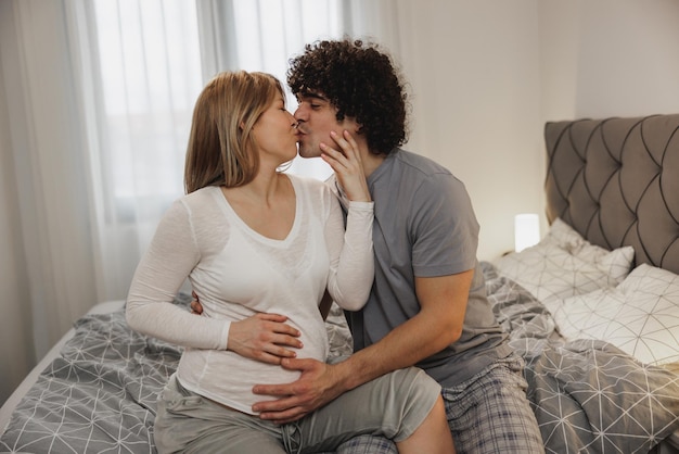 Glückliches schwangeres verliebtes Paar beim Entspannen auf einem Bett im Schlafzimmer.